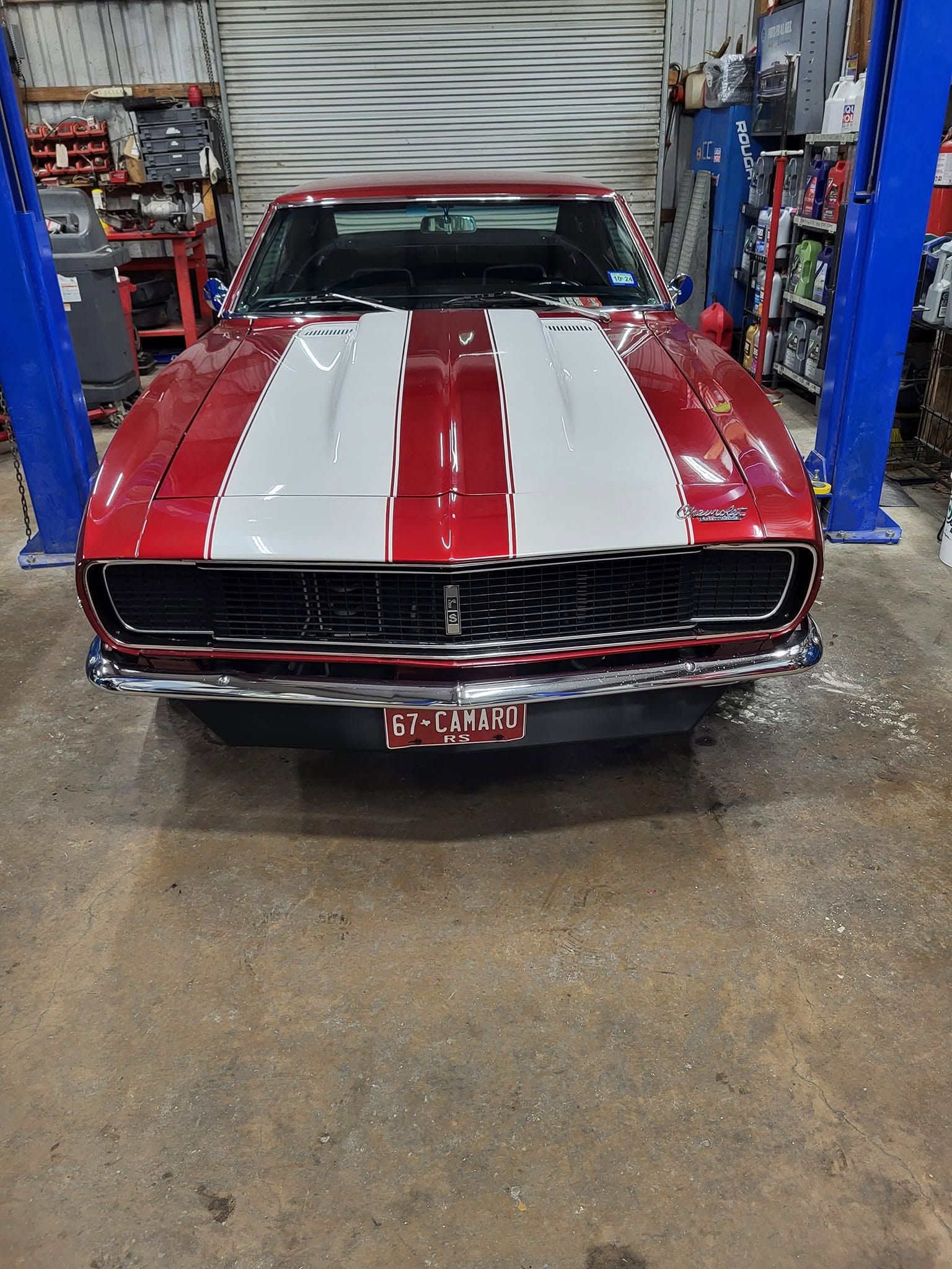Classic red muscle car with white racing stripes in an auto shop garage.