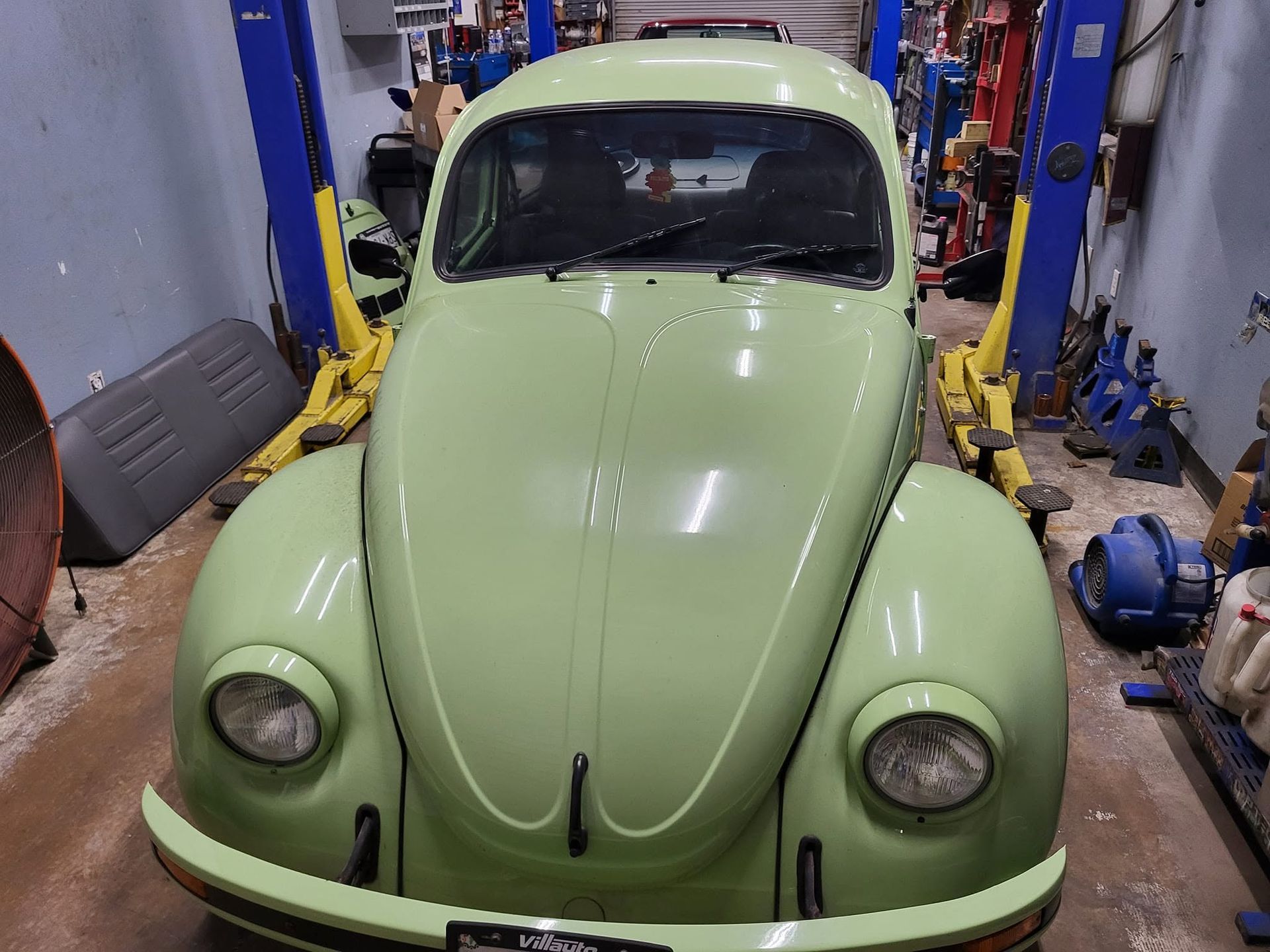 Light green classic Volkswagen Beetle in a garage on a vehicle lift
