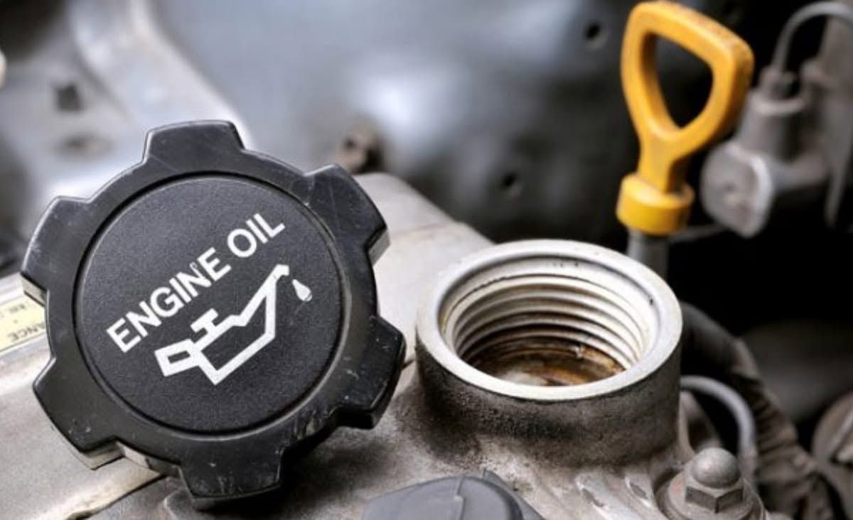 Car engine oil fill cap beside open oil filler opening and yellow dipstick handle