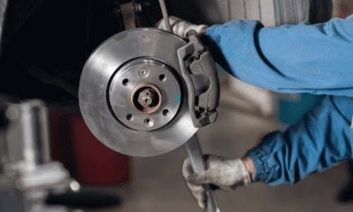 Close-up of a car brake rotor being serviced by a mechanic wearing blue gloves