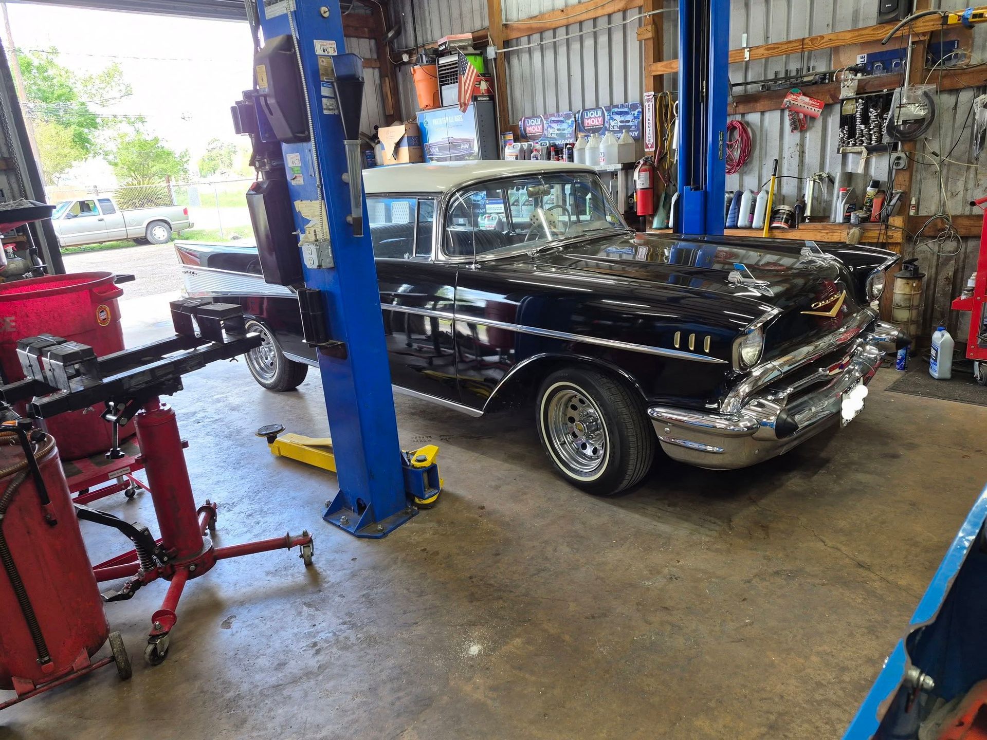 Classic black car in an auto repair shop with a lift and tools nearby.