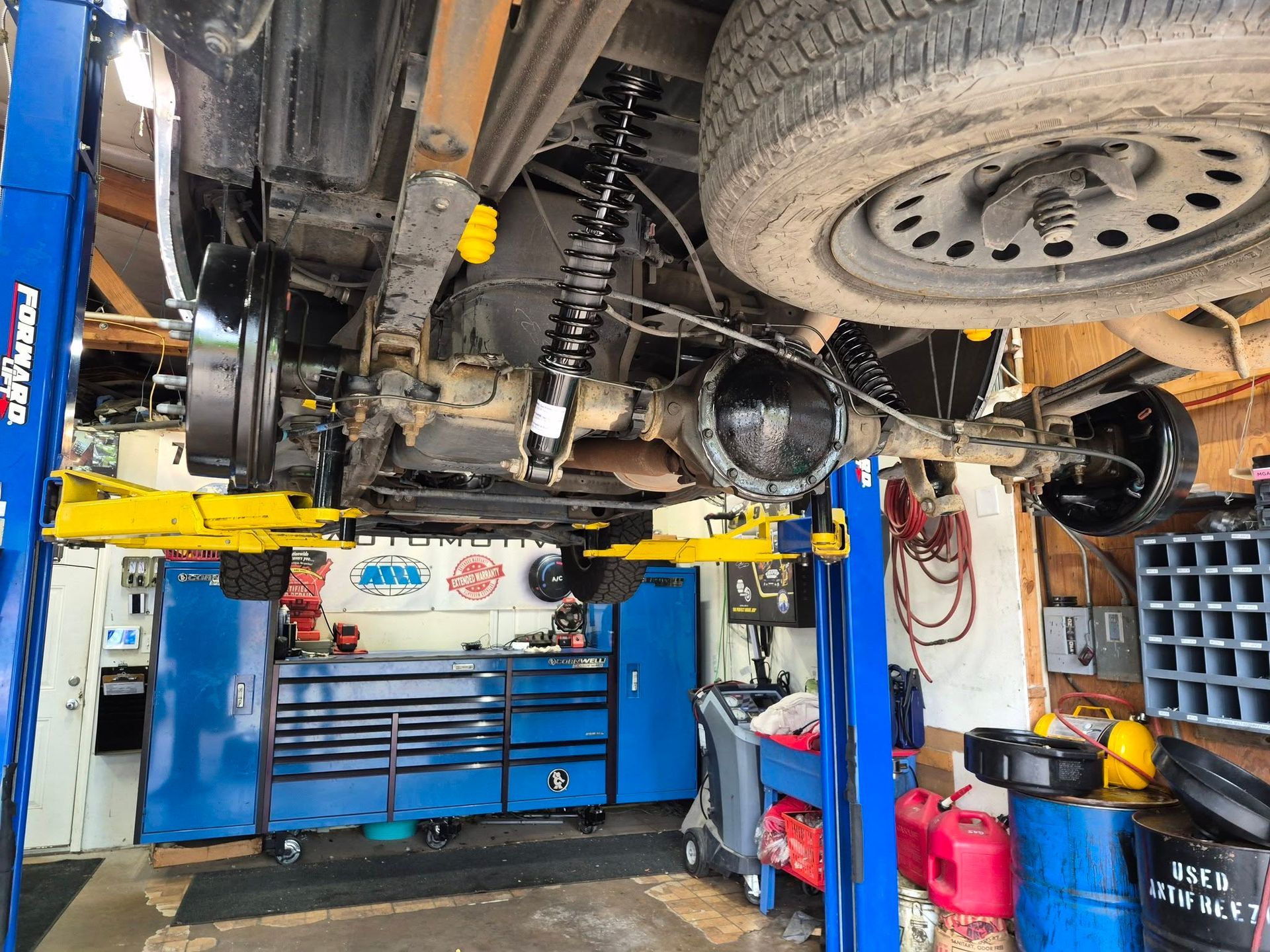Car lifted on a blue hydraulic auto lift inside a mechanic’s shop, with tools and equipment below