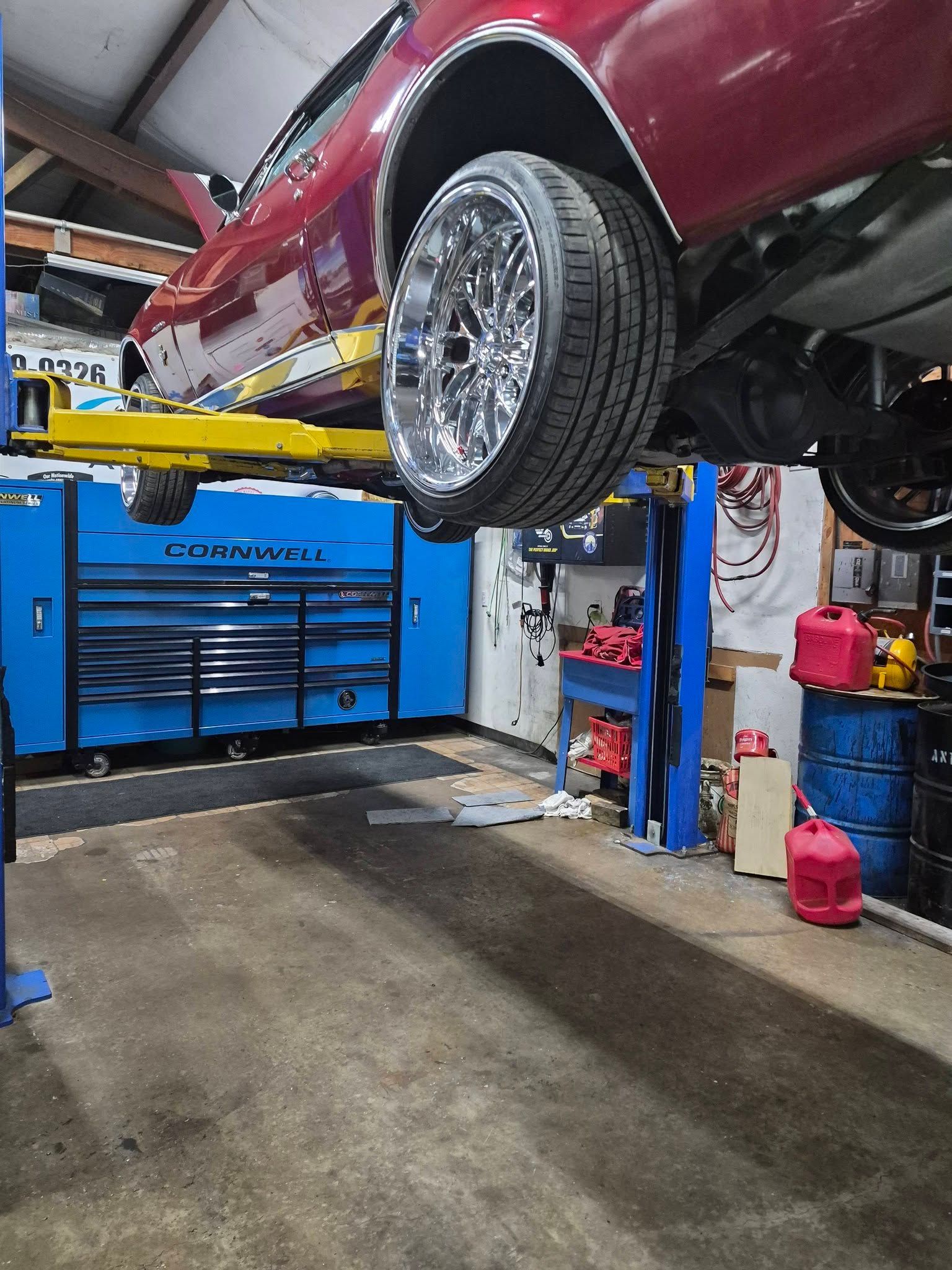 Red car lifted on a hydraulic jack in an auto repair garage, with tools and equipment nearby.