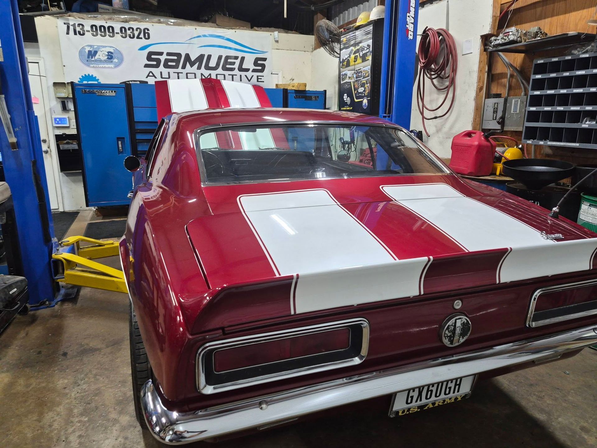 Red classic car with white racing stripes in a garage, viewed from the rear.