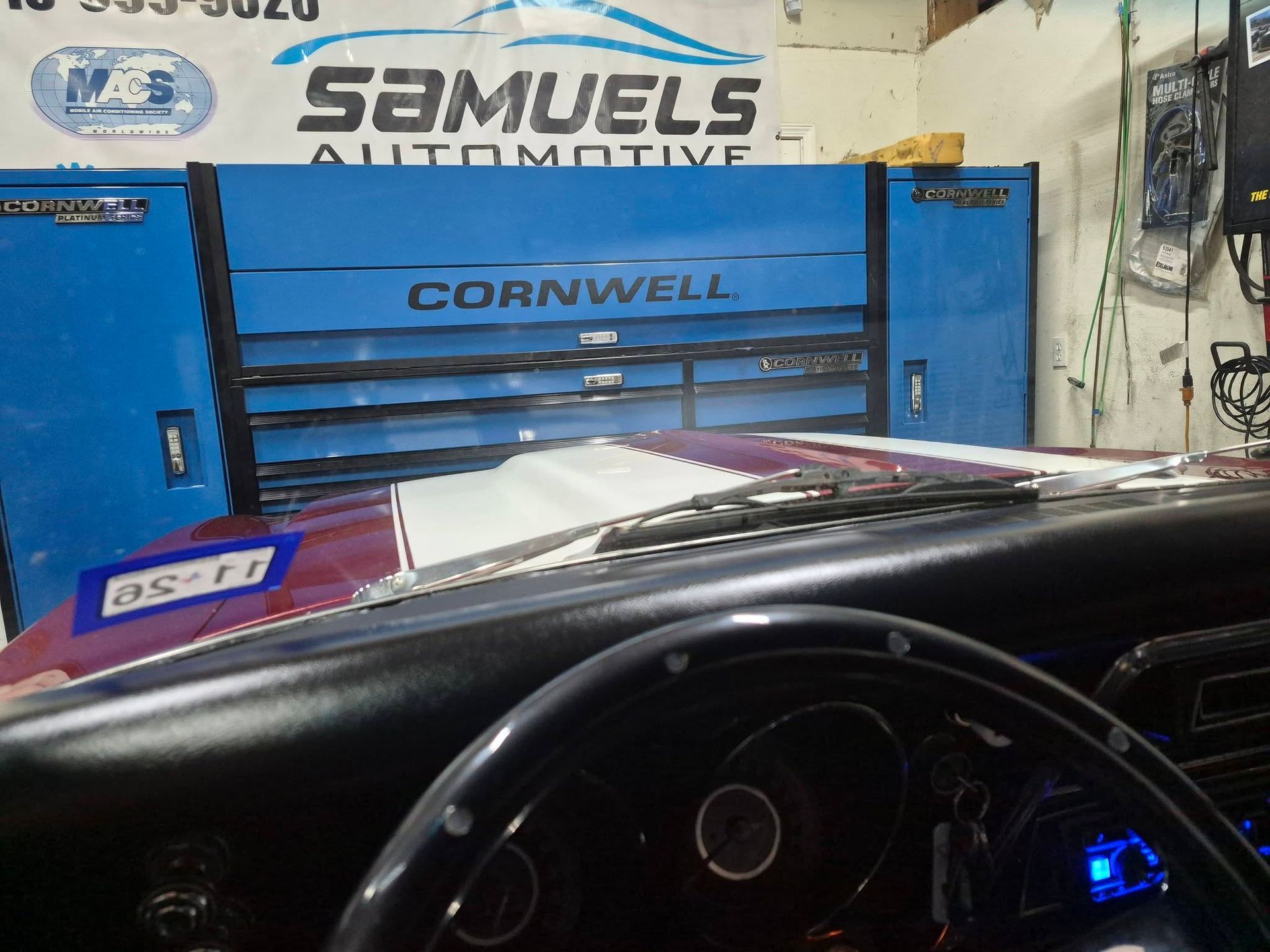Inside a car, facing a blue Cornwell tool chest and a Samuels Automotive shop sign.