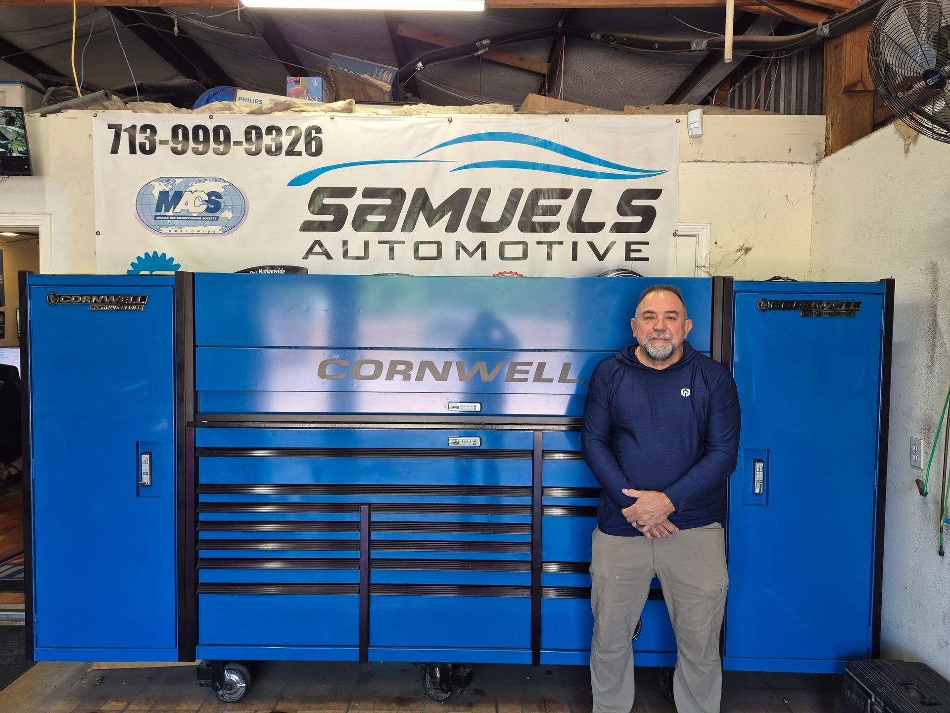 Man standing beside a blue Cornwell tool cabinet in Samuels Automotive garage under a banner sign