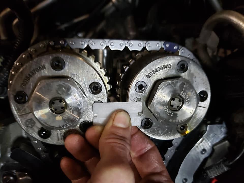 Hand adjusting a car engine timing chain between two metal cam gears with a wrench