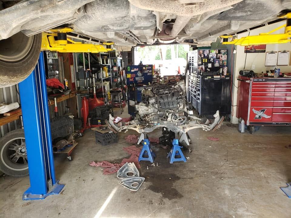 Auto repair shop with a car lifted overhead and engine parts spread on the floor between tool cabinets