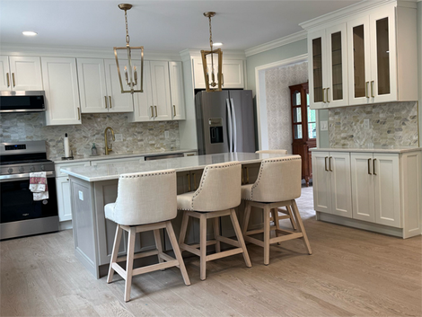 A kitchen with white cabinets and stools, and a large island.