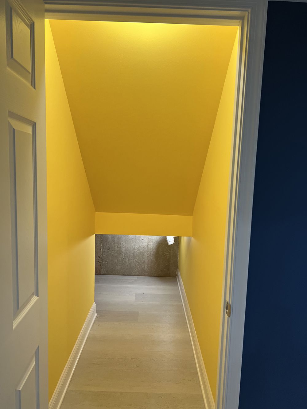 A hallway with yellow walls and a blue wall leading to a staircase.