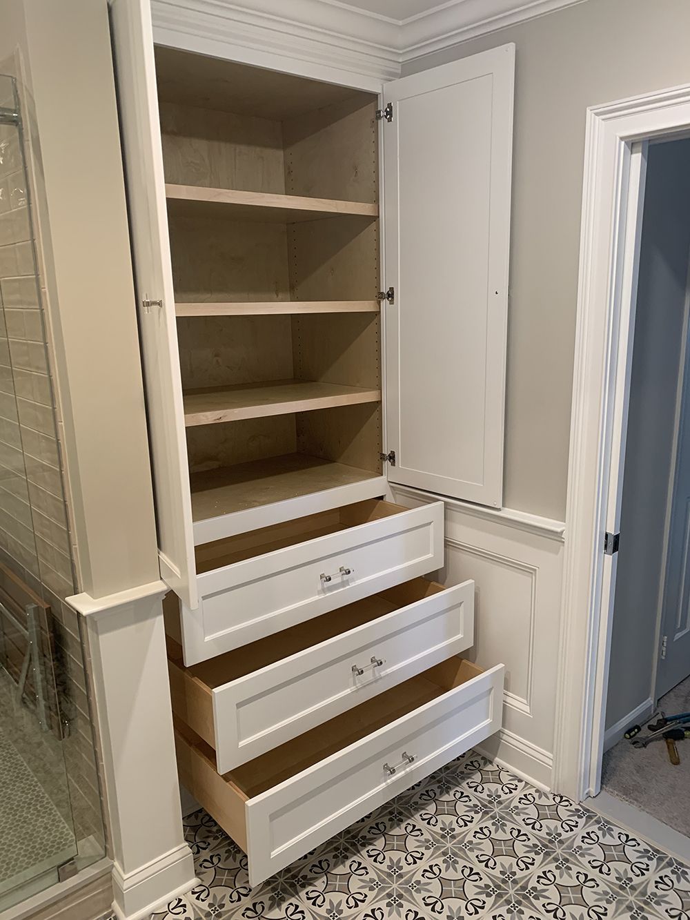 A white cabinet with drawers and shelves in a bathroom.