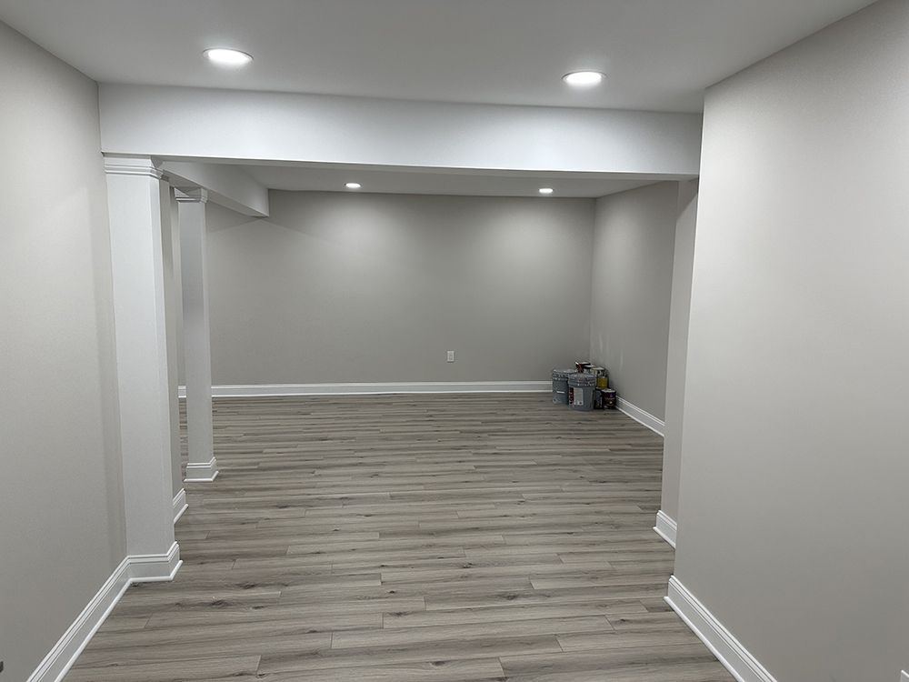 An empty basement with hardwood floors and white walls.
