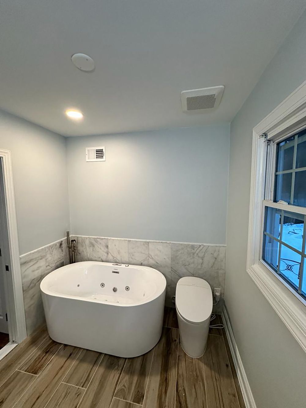 A bathroom with a tub, toilet and window.
