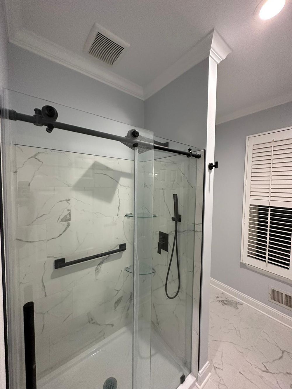 A bathroom with a sliding glass shower door and a window.