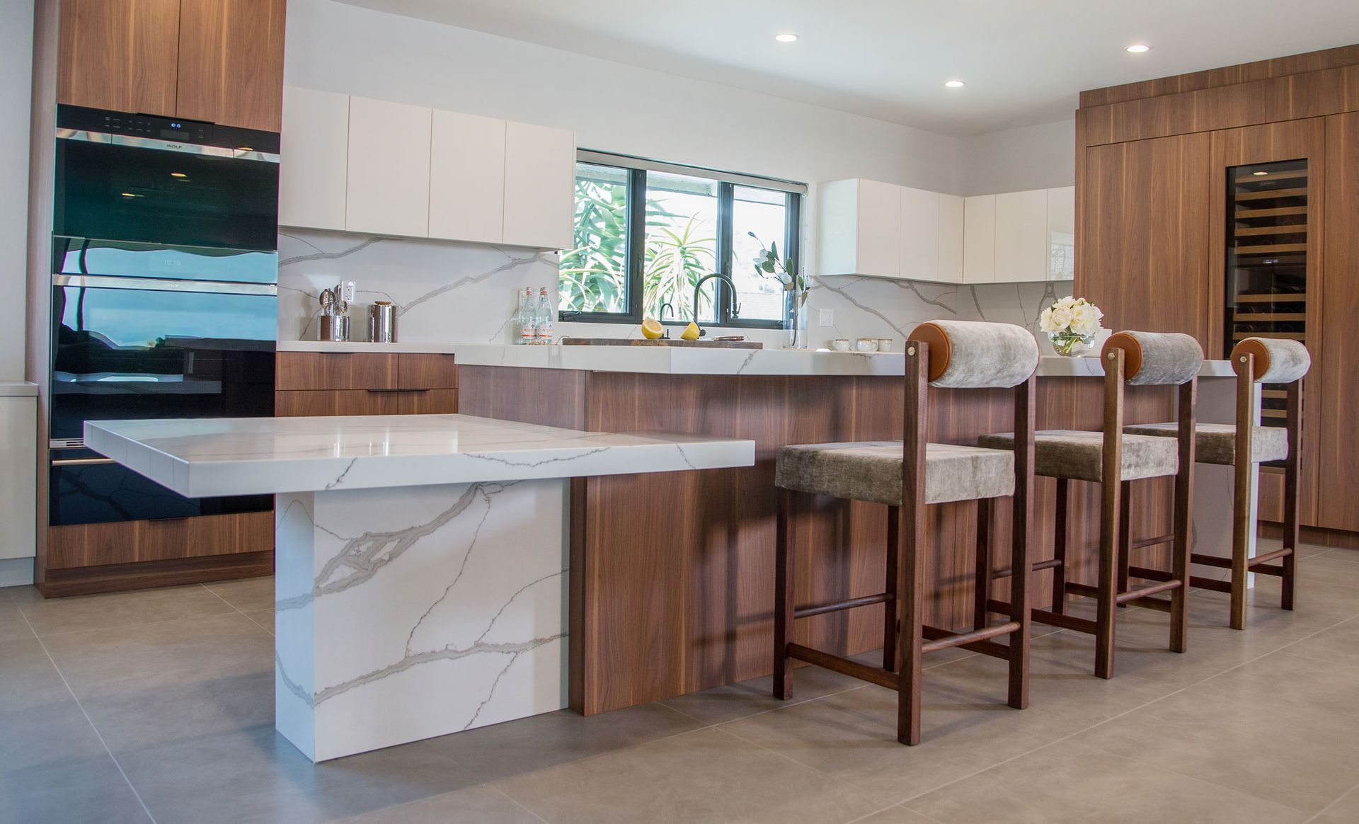 A kitchen with marble counter tops , wooden cabinets , and stools.