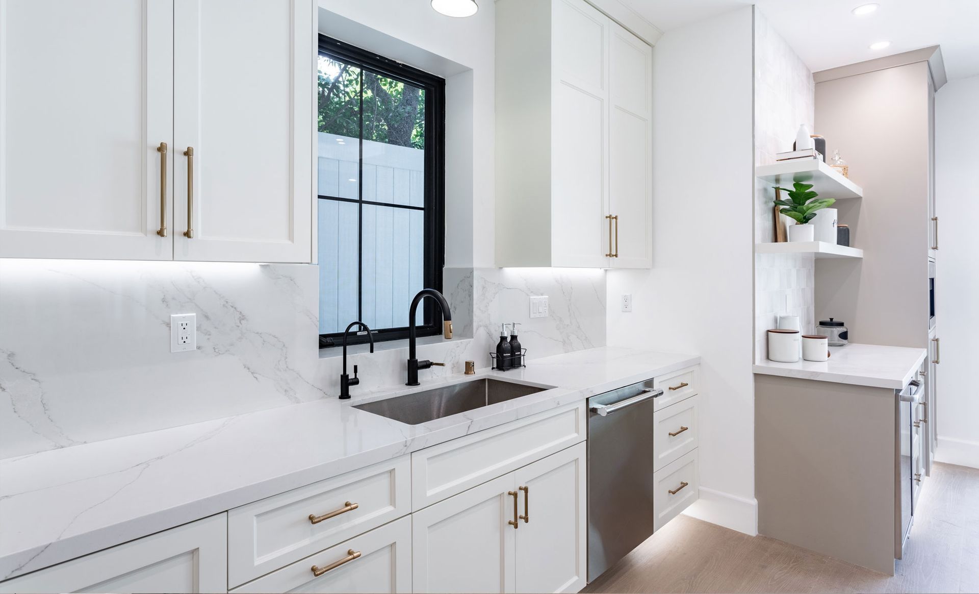 A kitchen with white cabinets , a sink , and a window.