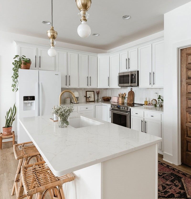 A kitchen with white cabinets , a large island , a refrigerator , a microwave , and a sink.