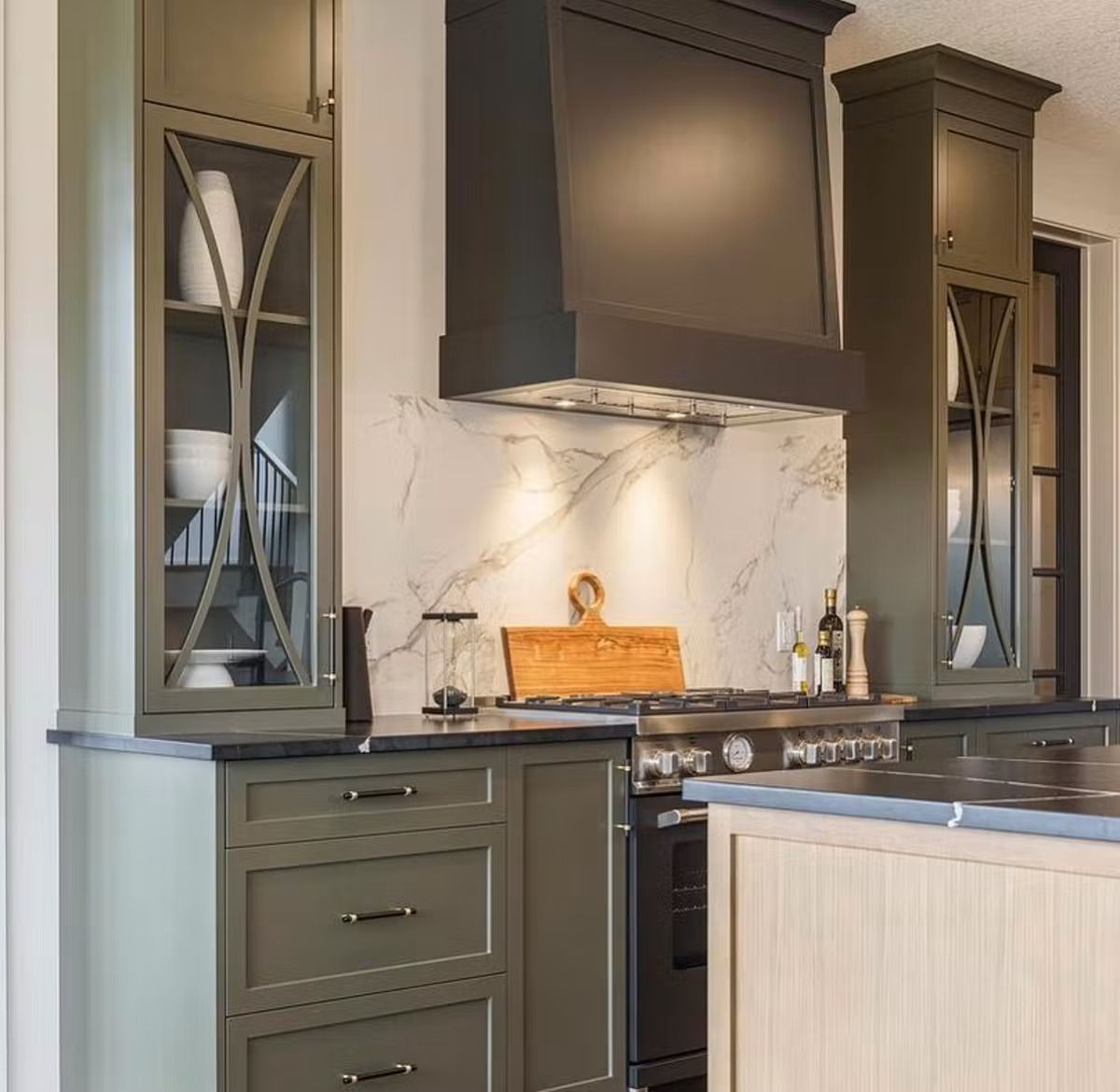 A kitchen with green cabinets , a stove , and a hood.