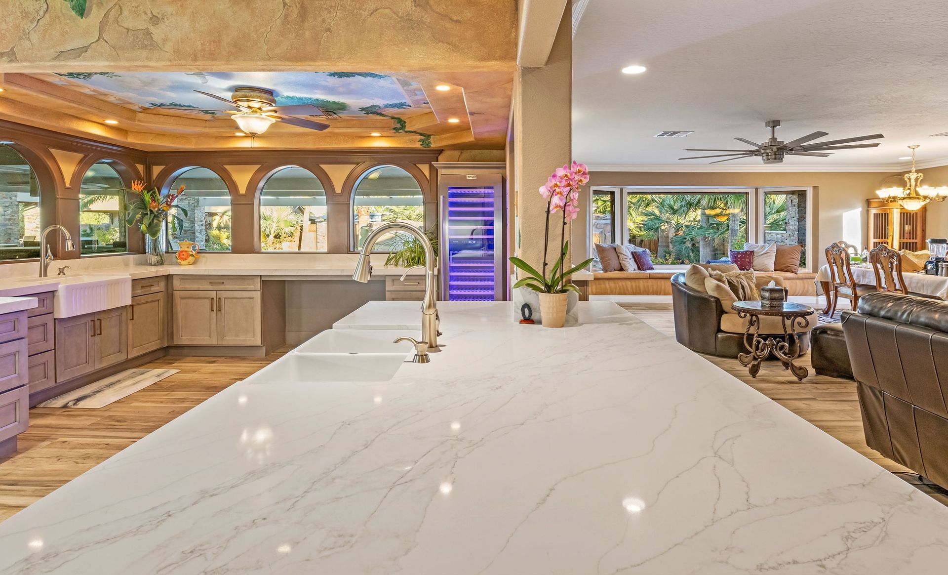 A kitchen with a large counter top and a living room in the background.