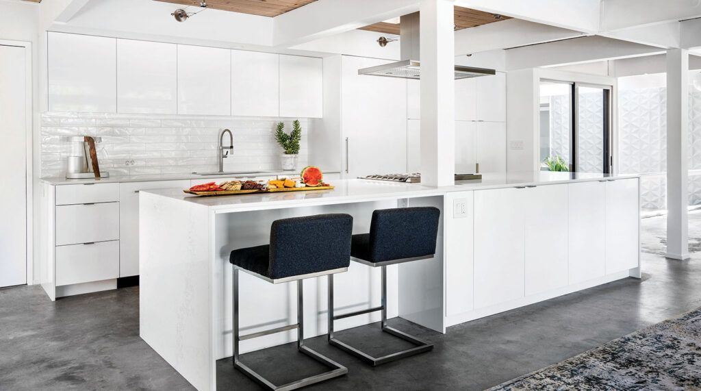 A kitchen with white cabinets , a large island , and two bar stools.
