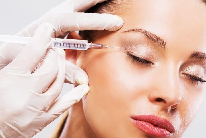 A woman is getting a botox injection in her forehead