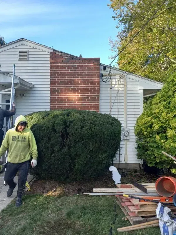 Man in green hoodie walks past a house with a brick chimney.