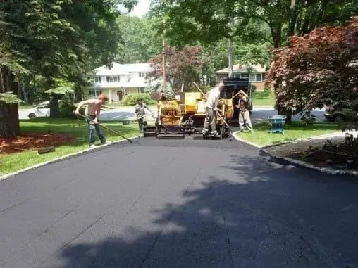 Asphalt paving crew resurfacing a residential driveway.