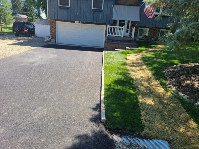 Asphalt driveway next to a strip of green grass and a house with a white garage door.