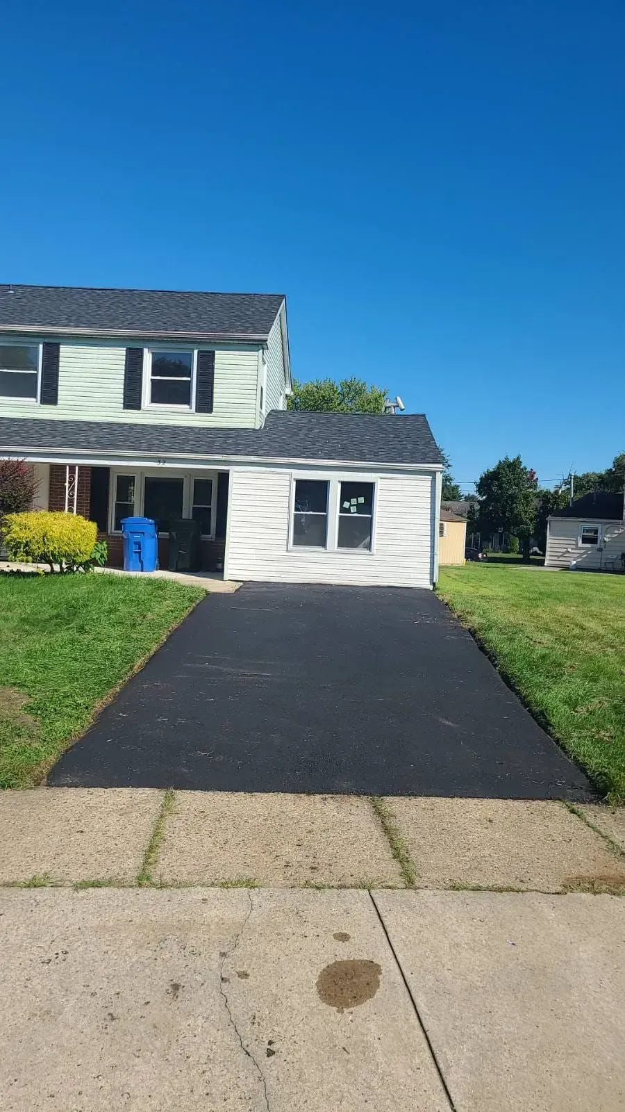 Two-story house with a dark asphalt driveway on a sunny day.
