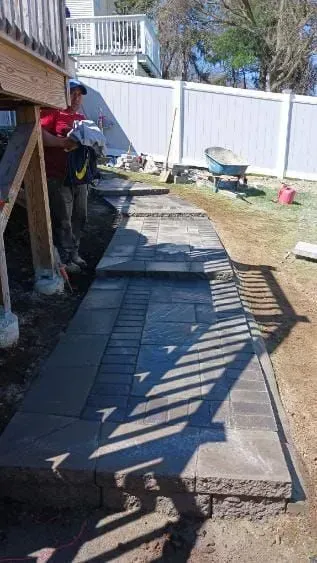 Construction worker laying pavers for a walkway next to a deck.