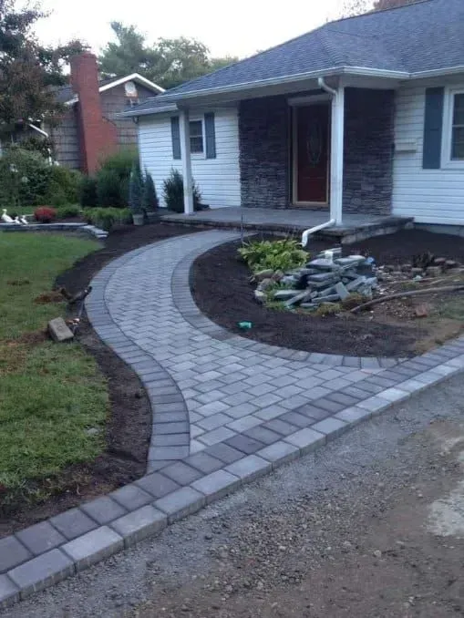 Stone walkway curves to a house entrance with landscaping.