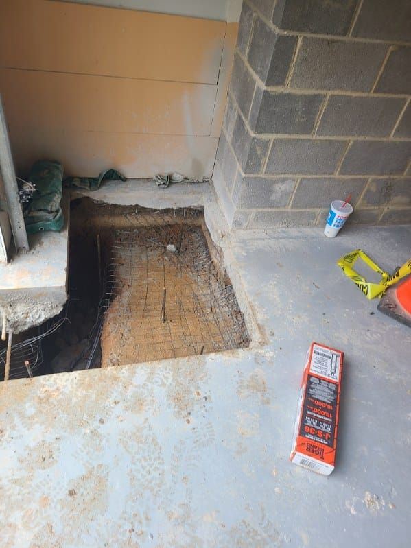 Construction site showing a concrete floor with a section removed, revealing rebar and dirt; a level is visible.