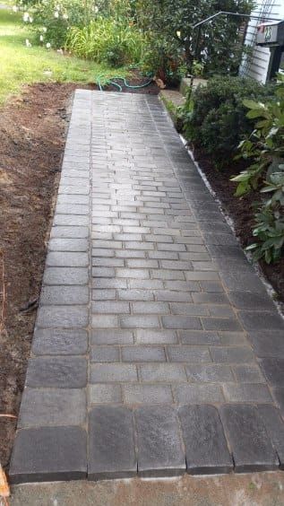 Brick pathway leading from garden to house. Dark gray bricks with light gray mortar.