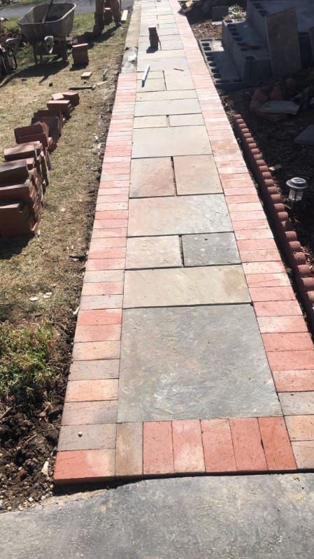 Brick pathway being constructed with a border of red bricks and large stone slabs.