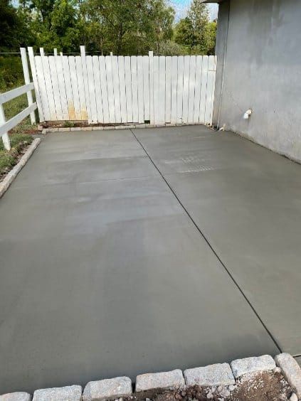 Newly poured concrete patio next to a white fence and a building's exterior wall.