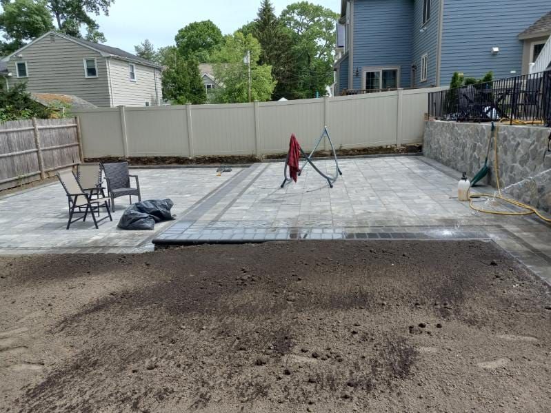 Backyard patio with gray pavers, fence, swing set, and dirt lawn.