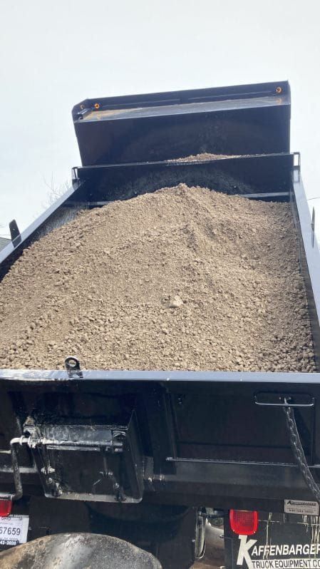 Dump truck bed full of gravel, raised against a light sky.