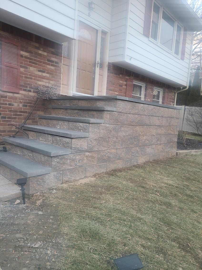 Exterior of a house with stone steps and retaining wall; brick facade and brown door.