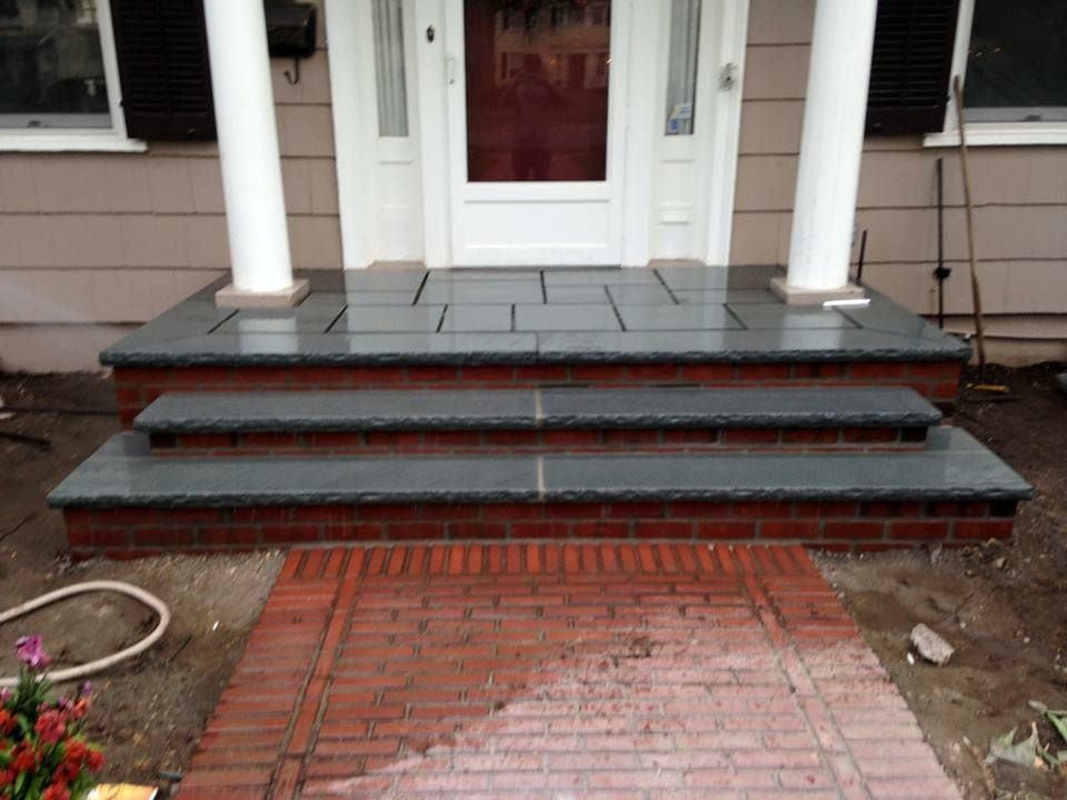 Brick and stone front porch with three steps. White columns support the roof.
