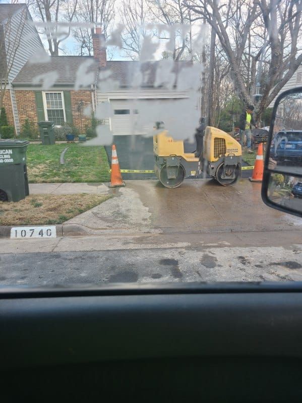 Road construction: A yellow asphalt roller compacting asphalt on a residential street in front of a house.