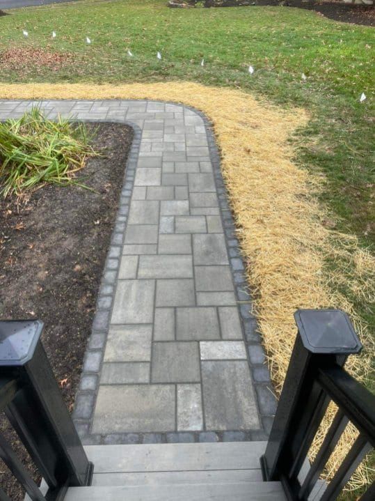 Brick walkway leading from steps to yard, bordered by grass and dark trim.