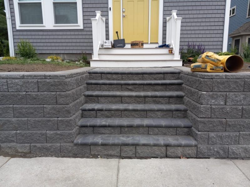 Grey brick steps leading up to a white porch with a yellow door. Retaining walls border the steps.
