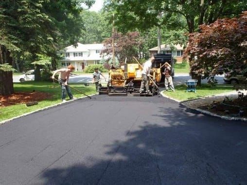 Asphalt paving a residential driveway, with workers and equipment in suburban area.