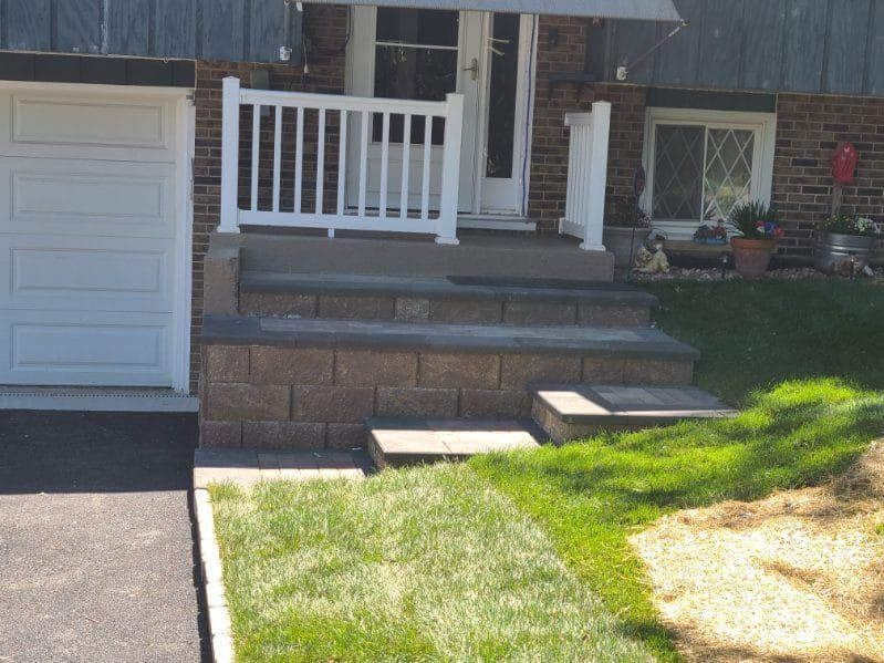 Brick steps leading to a white-railed porch with a door, next to a garage and grass.
