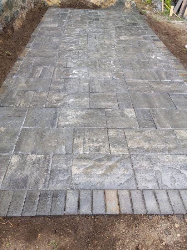 Newly installed rectangular stone patio, gray and tan bricks with brick border.