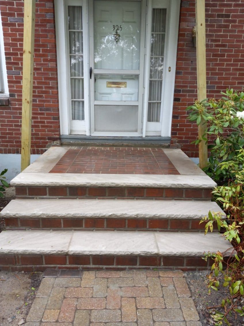Brick steps lead to a front door with a screen; brick walkway.