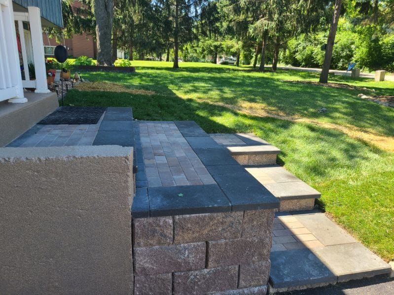 Stone steps and retaining wall leading up to a house porch, surrounded by green grass and trees.