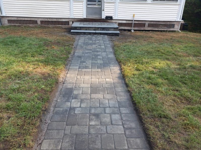 Brick walkway leading to a white house with a small set of steps. Green grass surrounds.