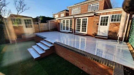 Backyard patio with steps, red brick walls, and a house with white doors.