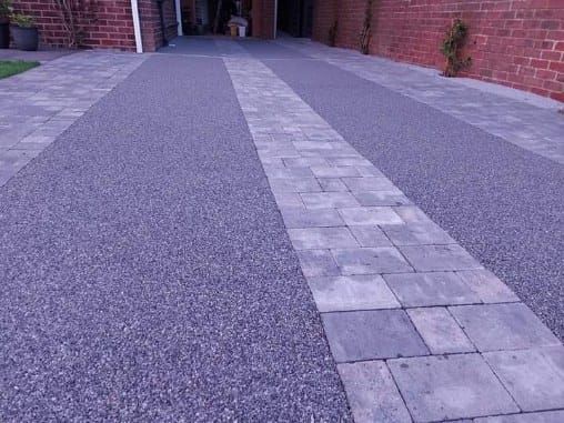Driveway with a gray pebble surface and a stone path down the center. Brick walls frame the sides.
